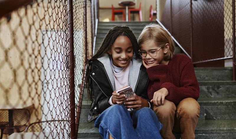 Two girls sitting on a staircase looking at a mobile